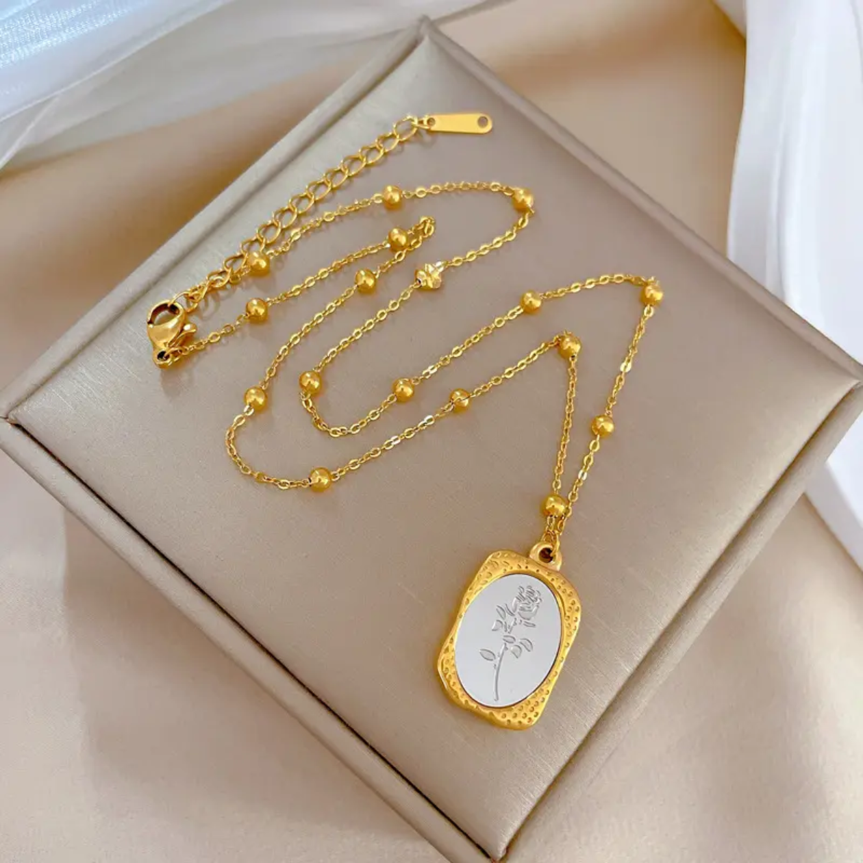 Gold necklace with a pendant on a beige jewelry box