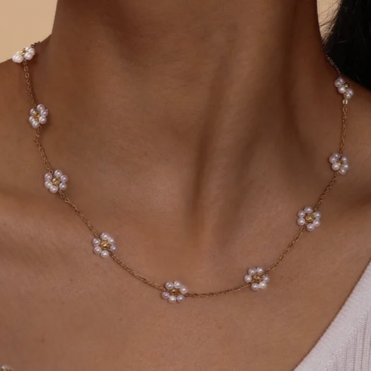 Necklace with floral pendants on a person wearing a light-colored top against a neutral background